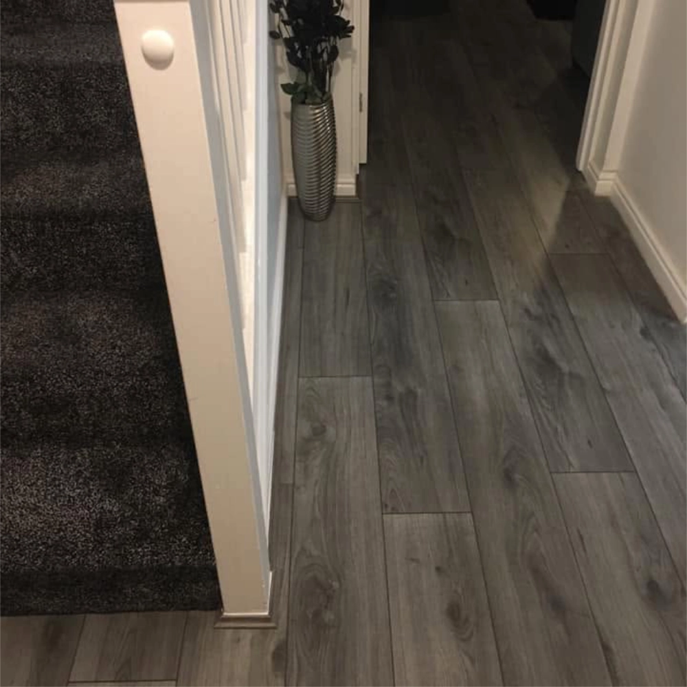 Grey wood-effect flooring fitted through a hallway beside a carpeted staircase