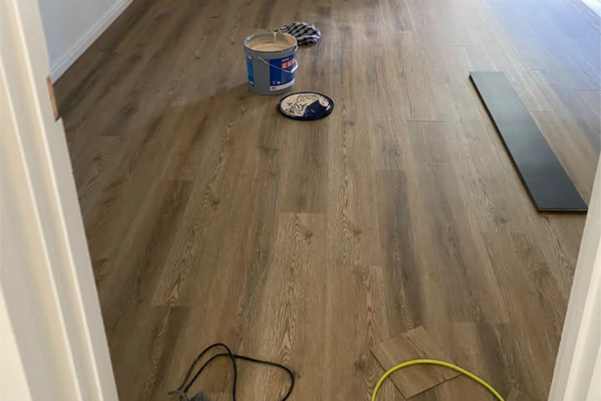 Wood-effect luxury vinyl tile flooring being fitted in a bright living room