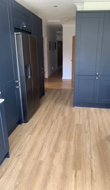 Light wood-effect flooring fitted in a modern kitchen with dark blue cabinets